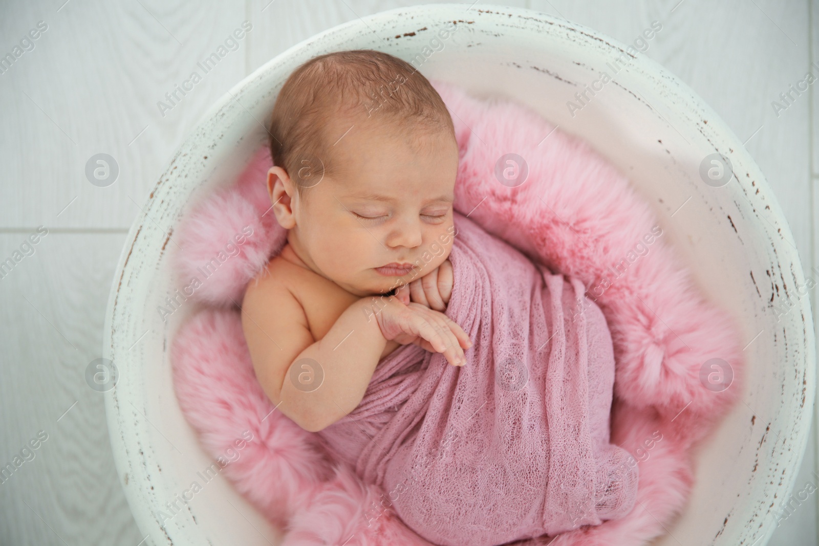 Photo of Adorable newborn girl lying in baby nest on light background, top view