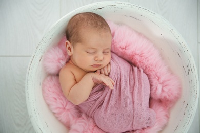 Adorable newborn girl lying in baby nest on light background, top view