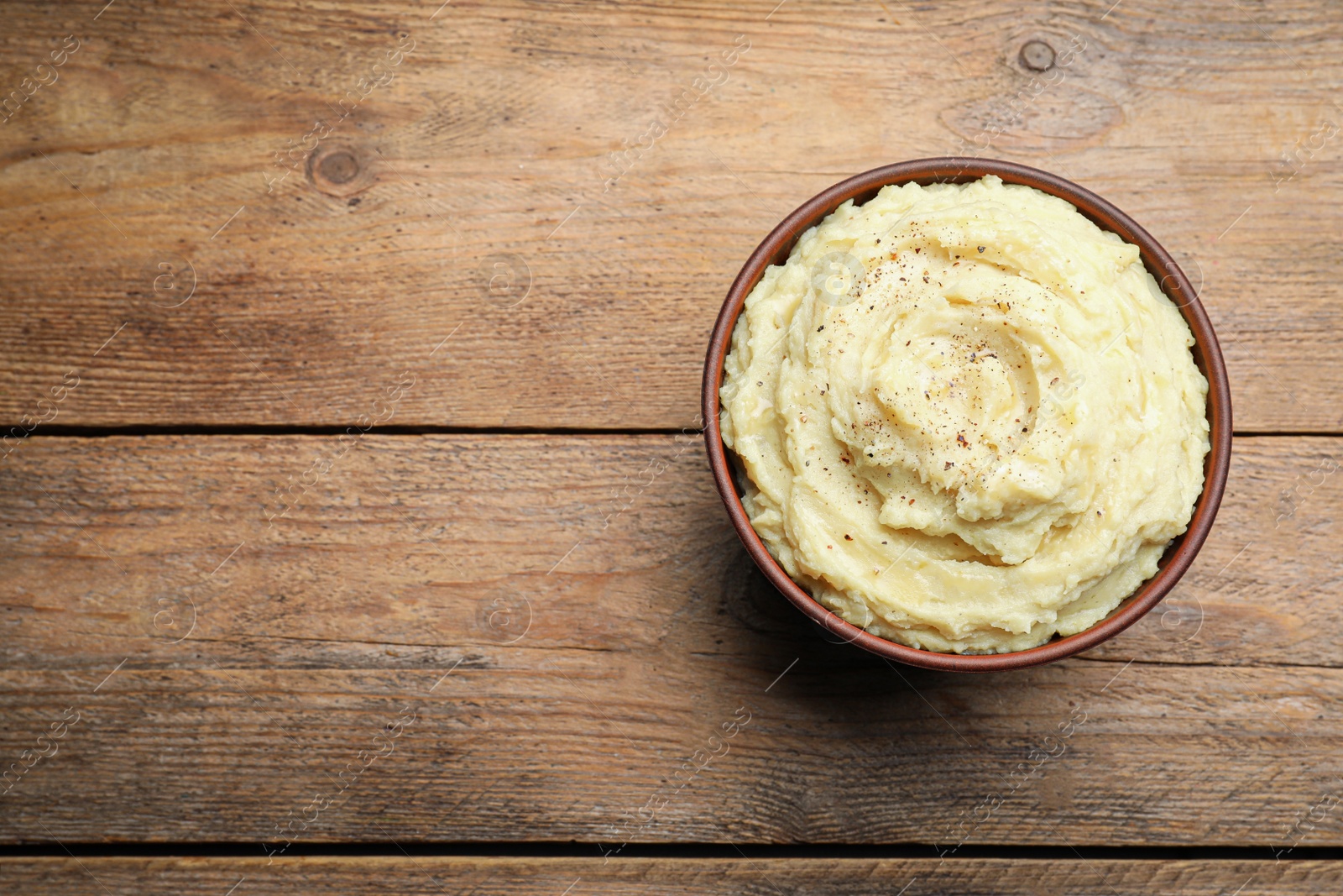 Photo of Bowl of tasty mashed potatoes with black pepper on wooden table, top view. Space for text