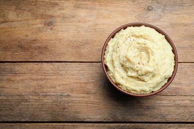 Photo of Bowl of tasty mashed potatoes with black pepper on wooden table, top view. Space for text