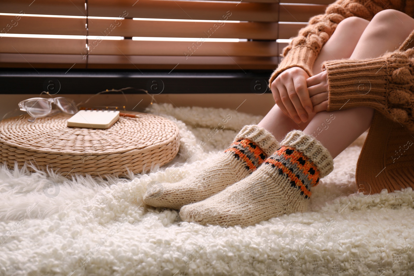 Photo of Woman wearing knitted socks on window sill indoors, closeup. Warm clothes