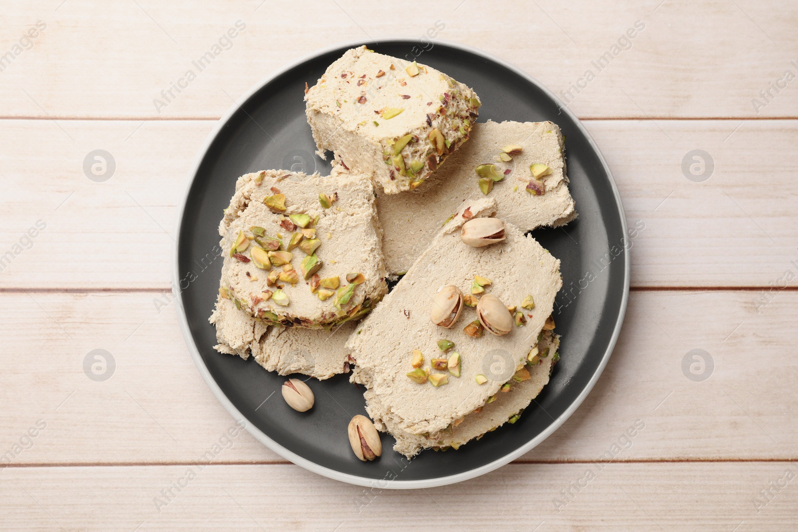 Photo of Pieces of tasty halva with pistachios on wooden table, top view