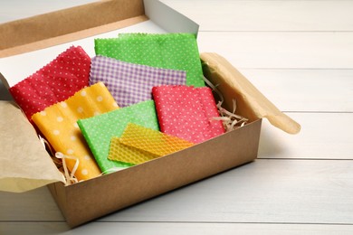 Photo of Colorful beeswax food wraps in box on white wooden table