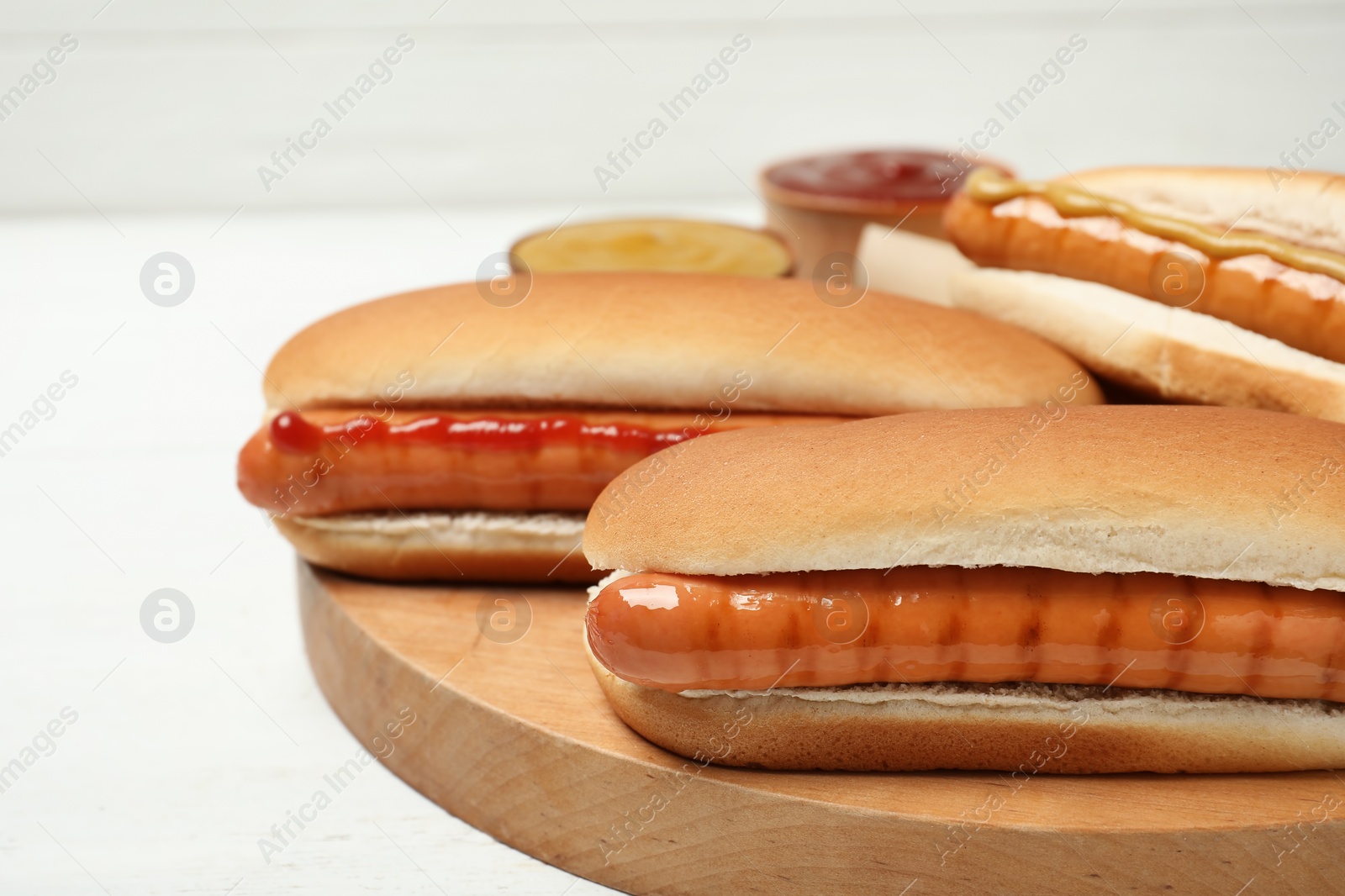 Photo of Tasty hot dogs on wooden board, closeup