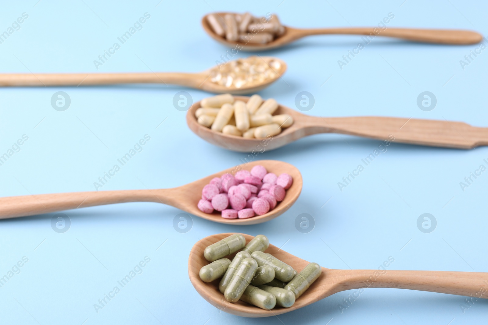 Photo of Different vitamin pills in wooden spoons on light blue background, closeup
