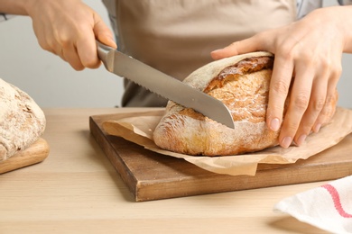Photo of Woman cutting freshly baked bread at wooden table, closeup