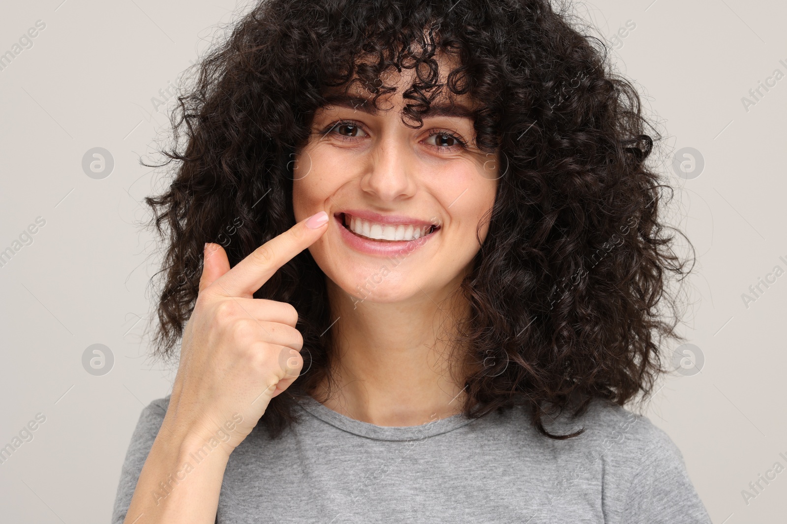 Photo of Young woman showing her teeth with whitening strip on light grey background