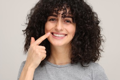 Photo of Young woman showing her teeth with whitening strip on light grey background