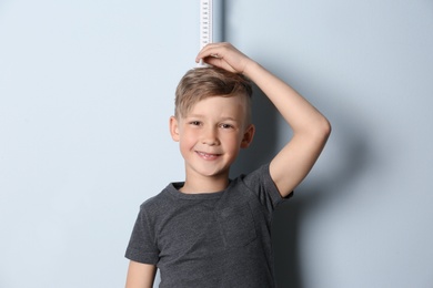 Photo of Little boy measuring his height on light background