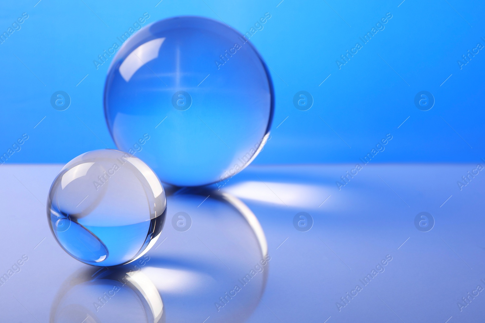 Photo of Transparent glass balls on mirror surface against blue background