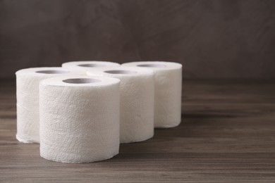 Photo of Soft toilet paper rolls on wooden table, closeup. Space for text