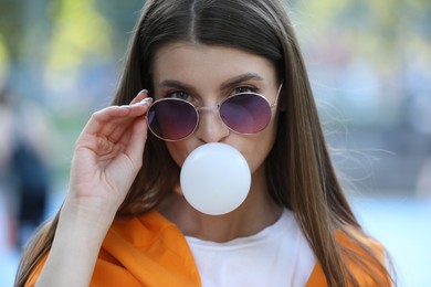 Beautiful young woman in sunglasses blowing bubble gum outdoors