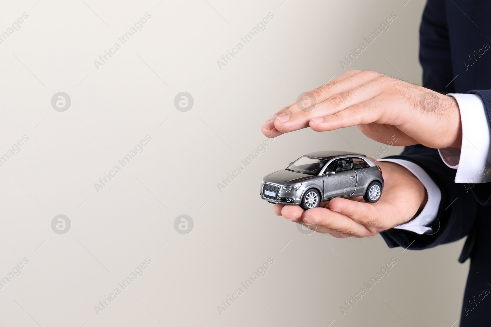 Photo of Male insurance agent holding toy car on light background, closeup. Space for text