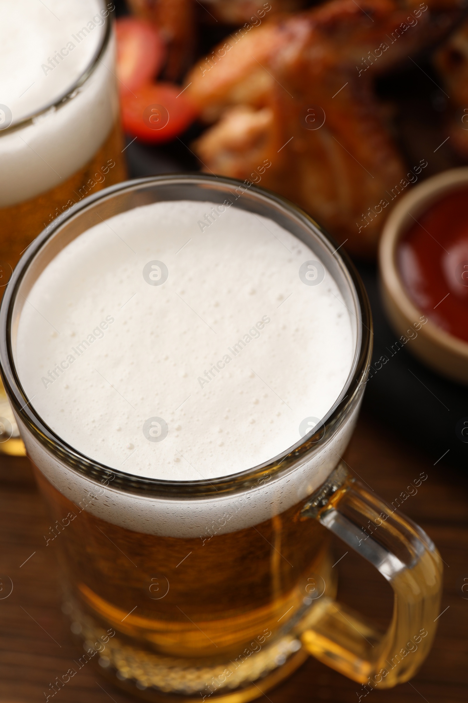 Photo of Mugs with beer and delicious baked chicken wings on wooden table, closeup