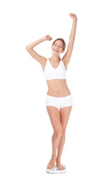 Happy young woman satisfied with her diet results using bathroom scales on white background