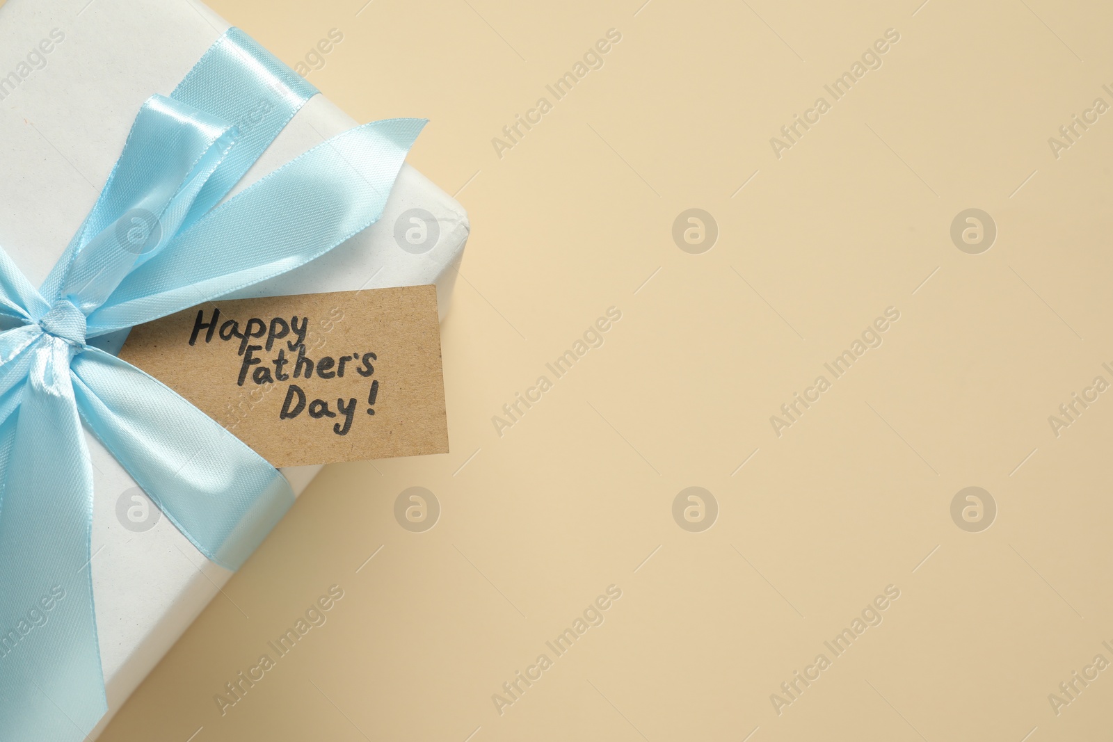 Photo of Card with phrase Happy Father's Day and gift box on beige background, top view. Space for text