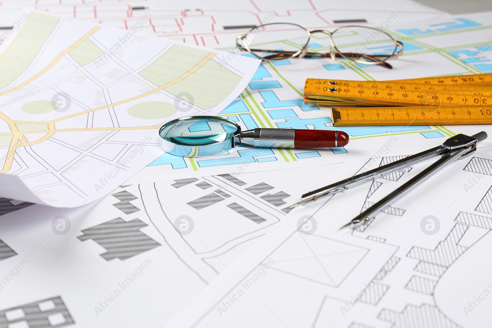 Photo of Office stationery, magnifying glass and folding ruler on cadastral maps of territory with buildings