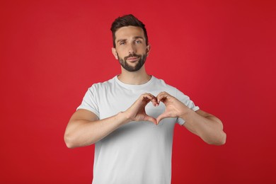 Photo of Man making heart with hands on red background