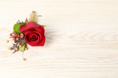 Photo of Stylish boutonniere with red rose on light wooden table. Space for text