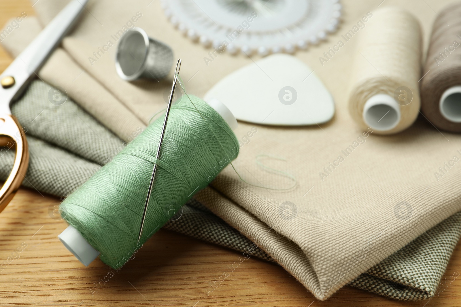 Photo of Spool of thread and sewing tools on wooden table, closeup