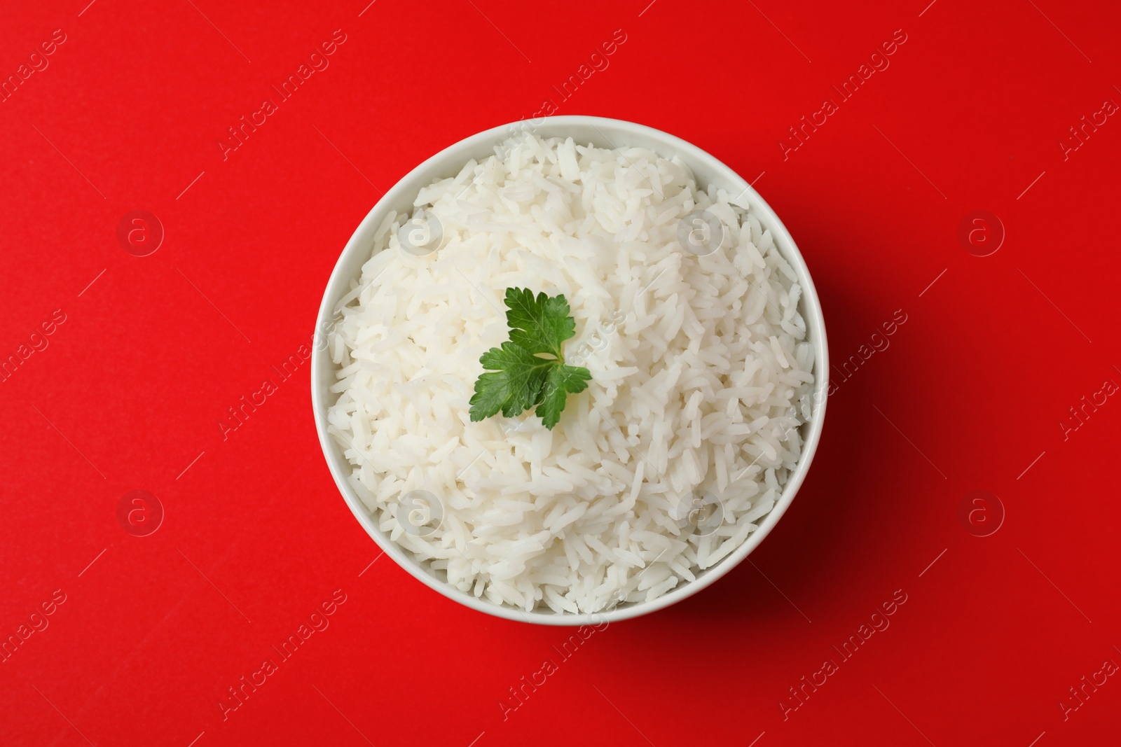 Photo of Bowl of tasty cooked rice with parsley on color background, top view