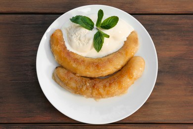 Plate with delicious fried bananas, ice cream and mint leaves on wooden table, top view