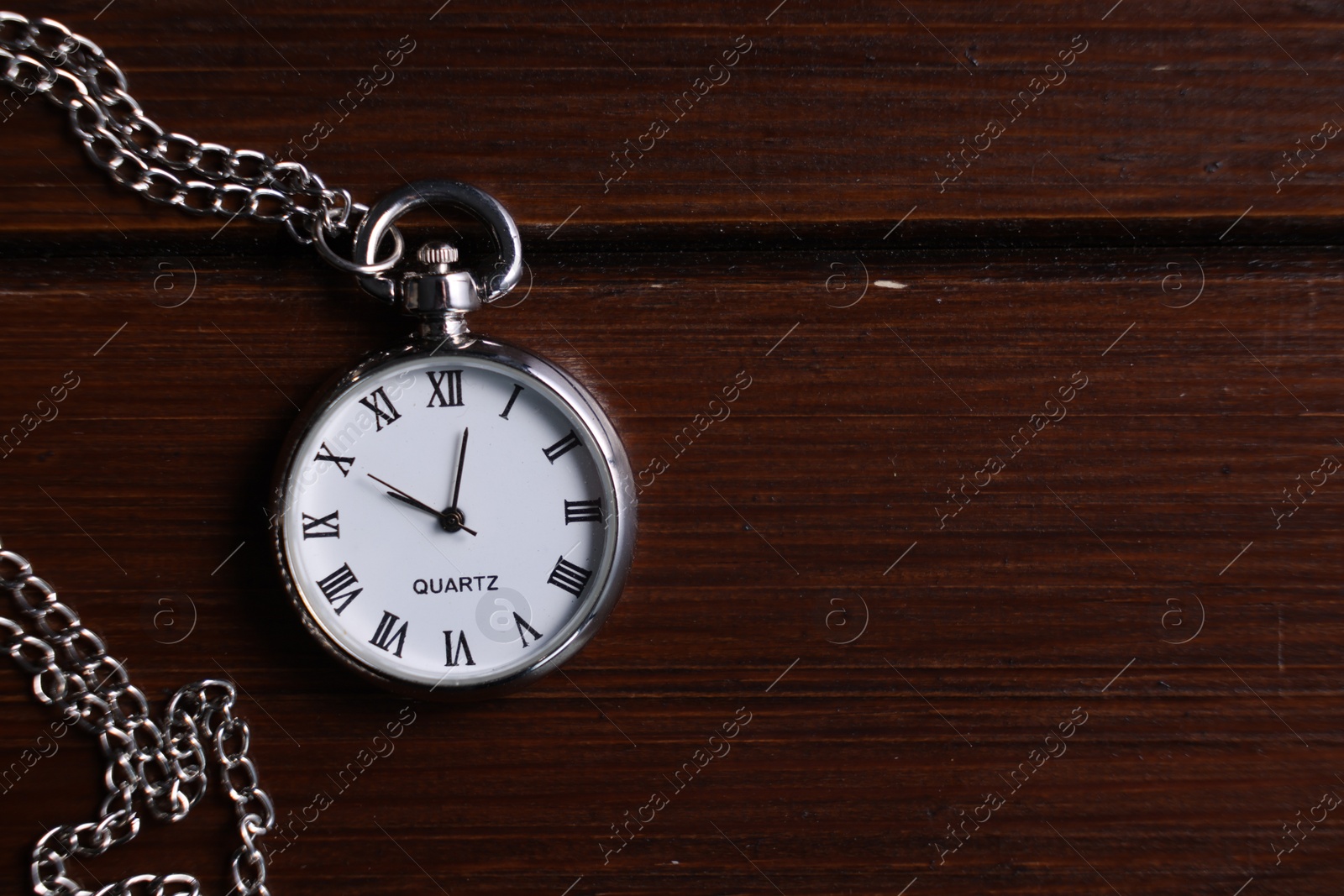 Photo of Silver pocket clock with chain on wooden table, top view. Space for text