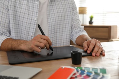 Professional designer with graphic tablet at wooden table, closeup