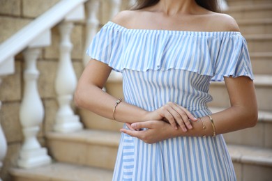 Photo of Young woman in stylish light blue striped dress on stairs outdoors, closeup