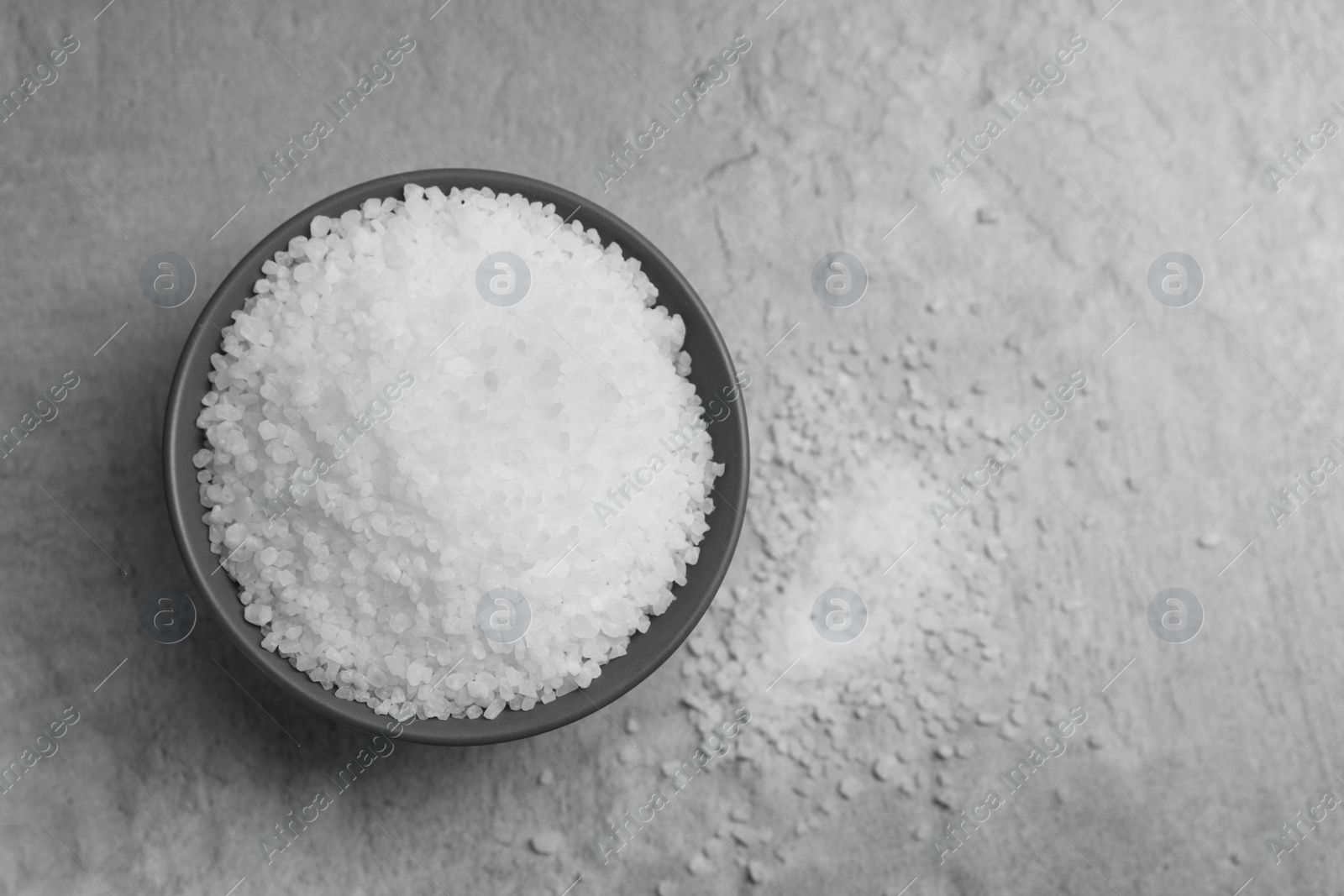 Photo of Natural salt in bowl on grey textured table, top view. Space for text