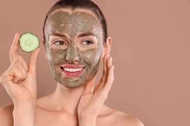 Beautiful woman with clay mask holding piece of cucumber on light brown background. Space for text