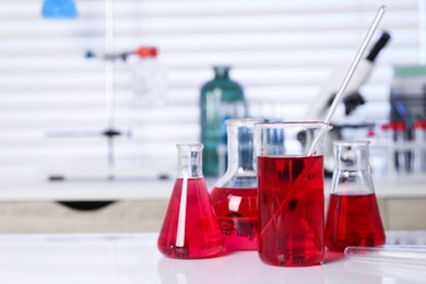 Photo of Laboratory analysis. Different glassware with red liquid on white table indoors. Space for text