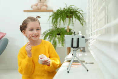 Photo of Cute little blogger with cosmetics recording video at home