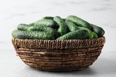 Photo of Fresh ripe cucumbers in wicker basket on marble table