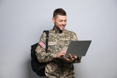 Photo of Cadet with backpack and laptop on light grey background. Military education