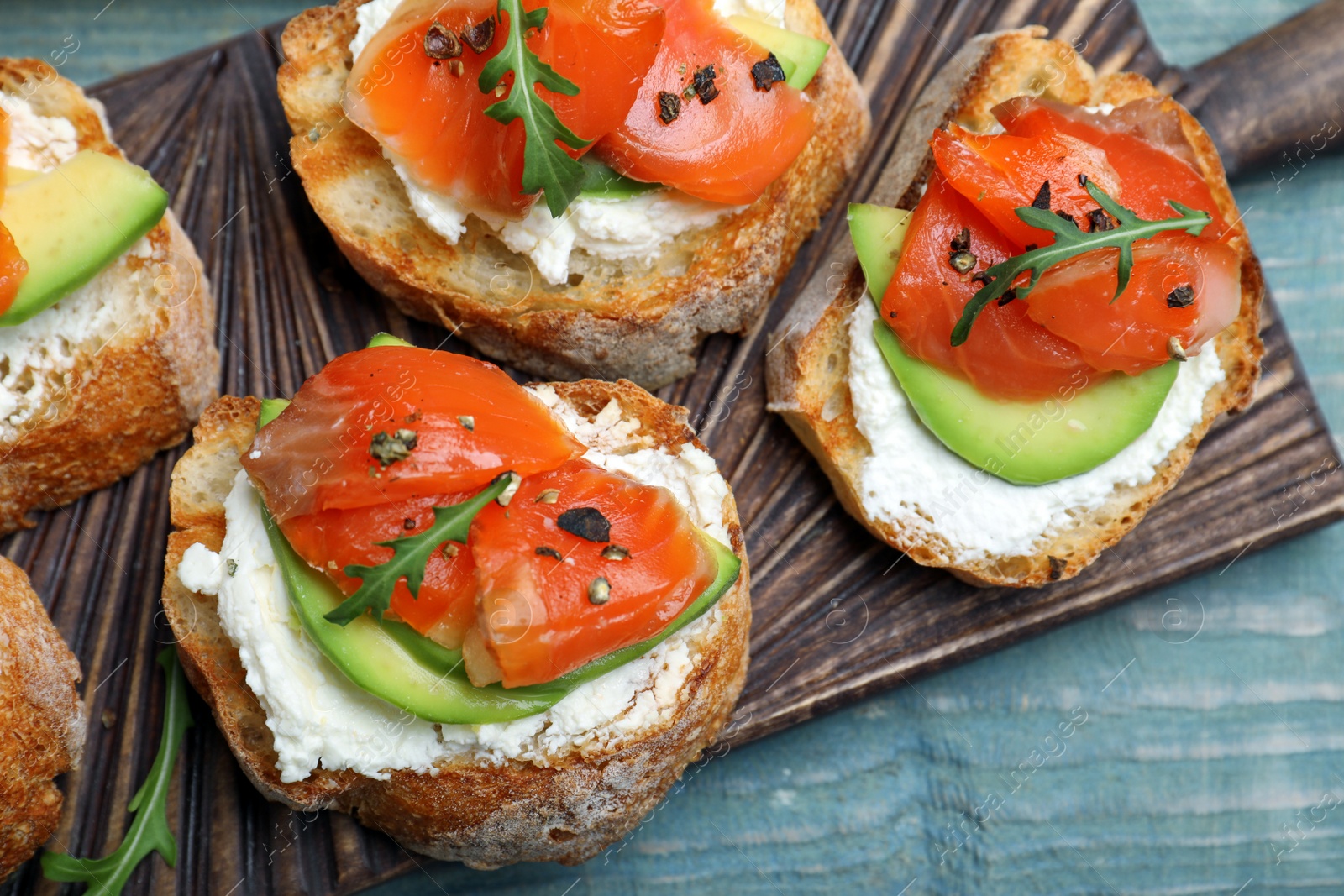 Photo of Delicious sandwiches with cream cheese, salmon, avocado and arugula on light blue wooden table, closeup