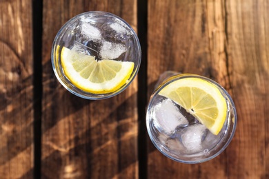 Photo of Glasses of refreshing drink with ice and lemon for hot summer day on wooden table, top view