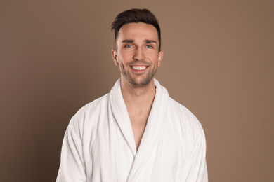 Photo of Happy young man in bathrobe on brown background