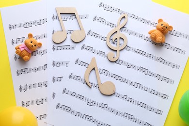 Photo of Baby songs. Music sheets, wooden notes, toy bears and balls on yellow background, top view