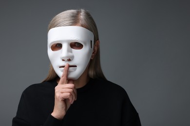 Photo of Multiple personality concept. Woman in mask showing hush gesture on gray background, space for text