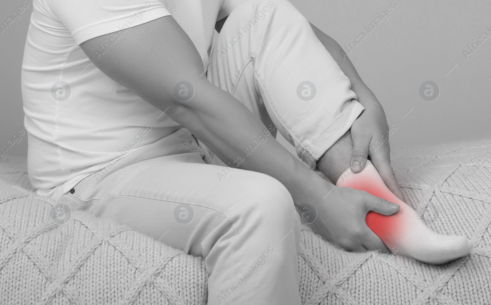 Image of Man suffering from pain in ankle on bed, closeup. Black and white effect