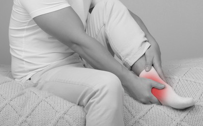 Man suffering from pain in ankle on bed, closeup. Black and white effect