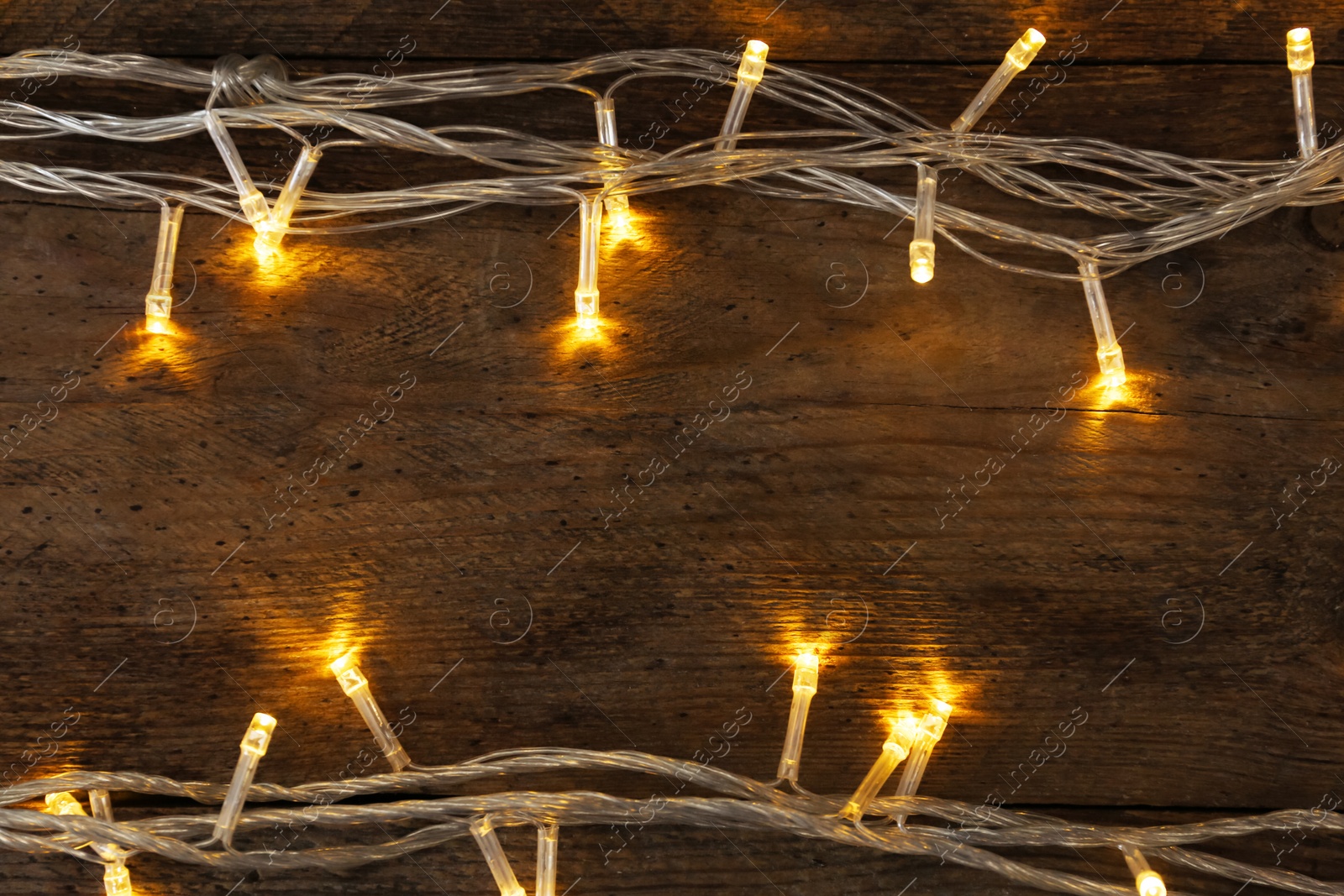 Photo of Glowing Christmas lights on wooden background, top view. Space for text