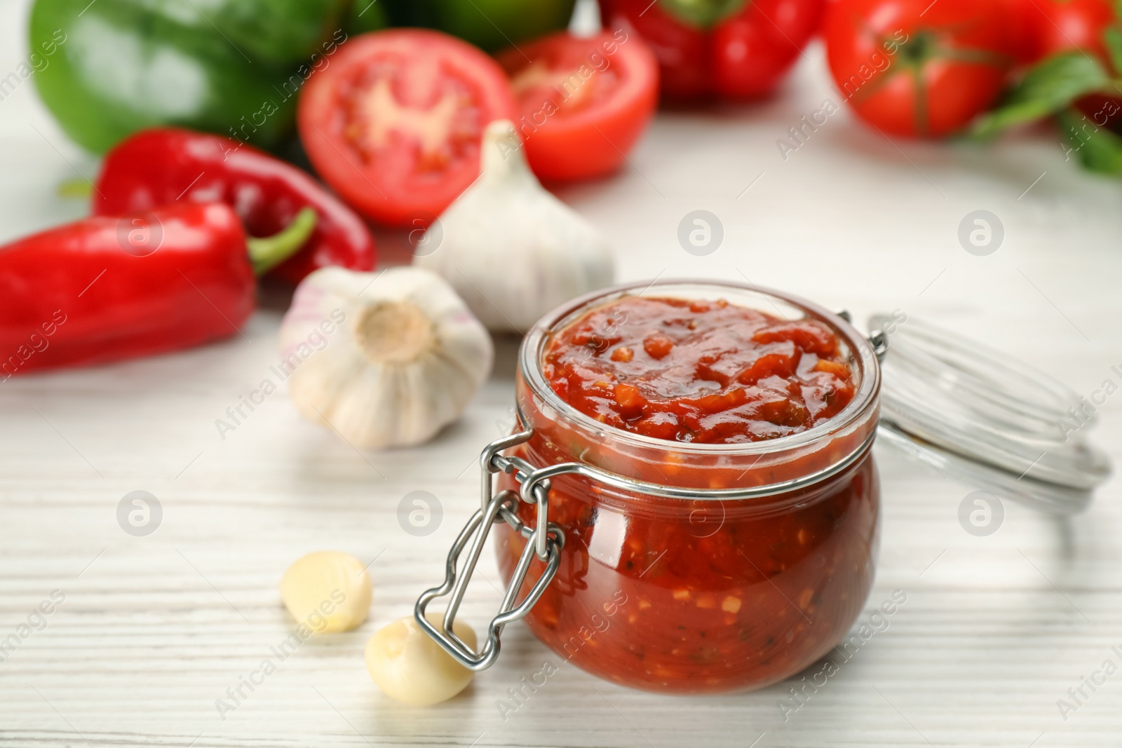 Photo of Glass jar of tasty adjika and ingredients on white wooden table