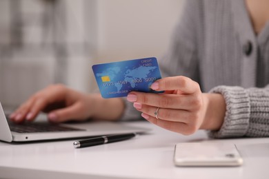 Woman with credit card using laptop for online shopping at white table, closeup