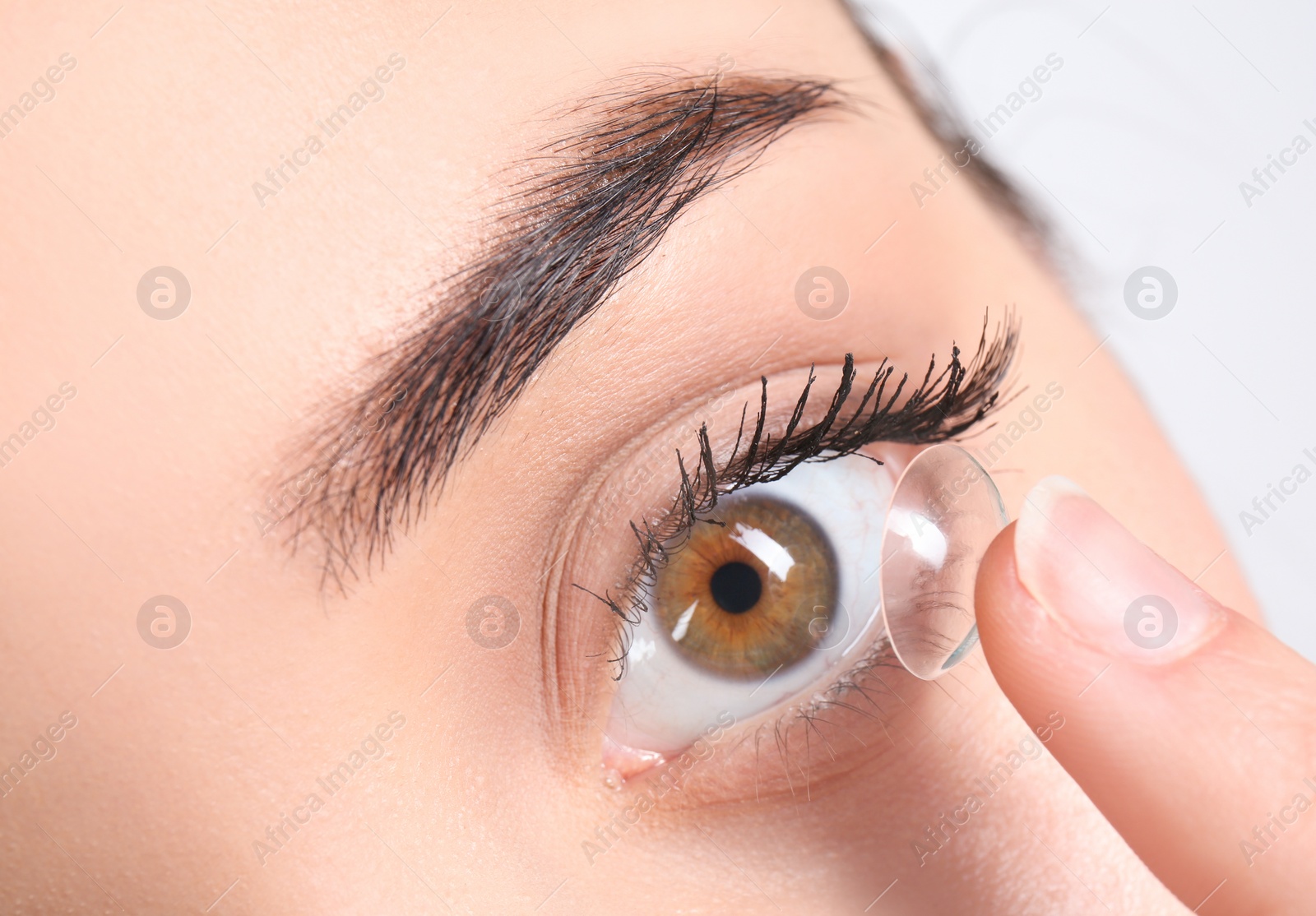 Photo of Young woman putting contact lens in her eye, closeup