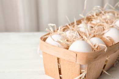 Basket with raw chicken eggs on wooden table. Space for text