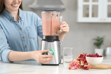 Beautiful young woman preparing tasty smoothie at white table in kitchen, closeup. Space for text