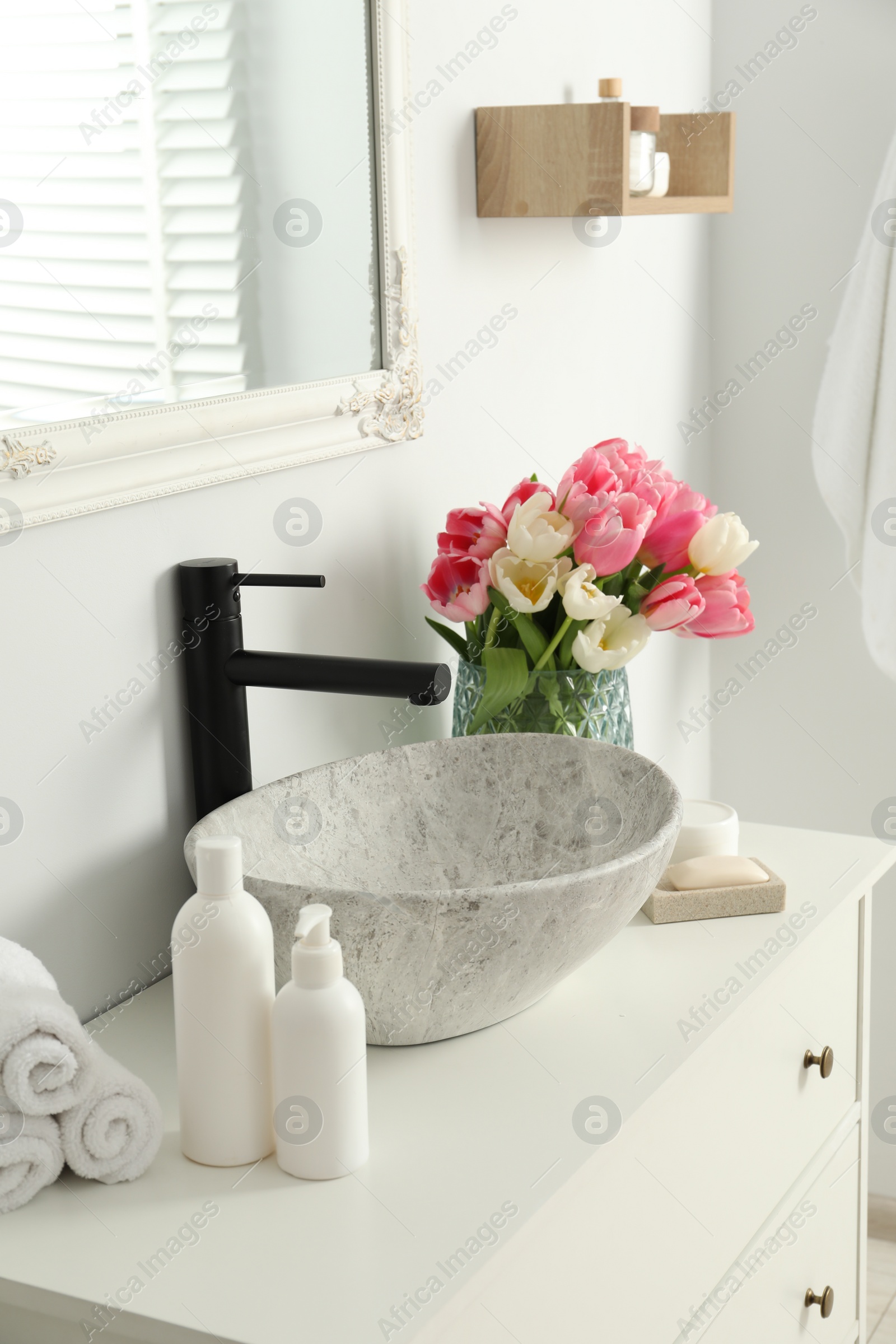 Photo of Vase with beautiful pink tulips and toiletries near sink in bathroom