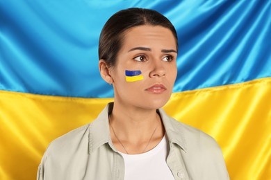 Sad young woman with face paint near Ukrainian flag